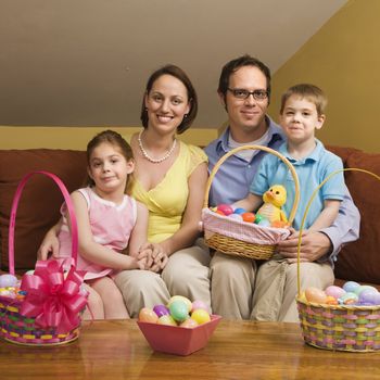 Caucasian family on couch holding Easter basket and looking at viewer.