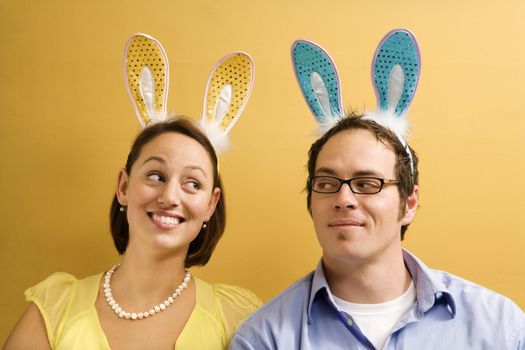Caucasian mid adult couple wearing rabbit ears and looking at each other.