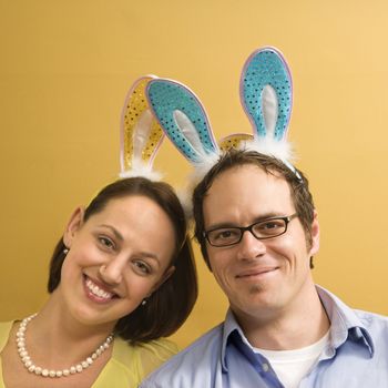 Caucasian mid adult couple wearing rabbit ears and looking at viewer.