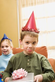 Caucasian boy wearing party hat pouting and looking at viewer.