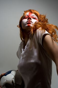 English football makeup girl holding worn soccer ball, looking directly into camera