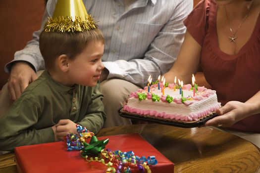 Caucasian boy in party hat with Birthday cake and family.