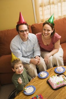 Caucasian boy and parents in party hats eating birthday cake.