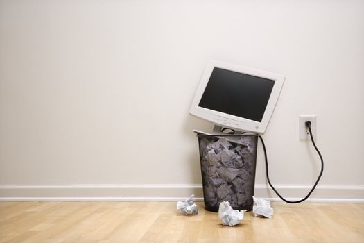 Computer monitor in trash can surrounded by crumpled up paper.