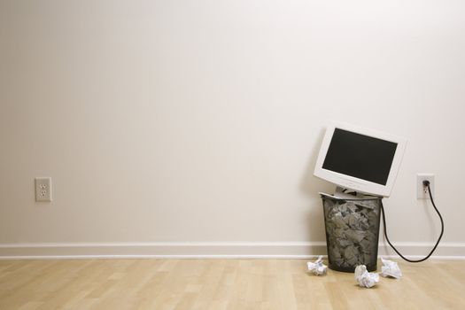 Computer monitor in trash can surrounded by crumpled up paper.