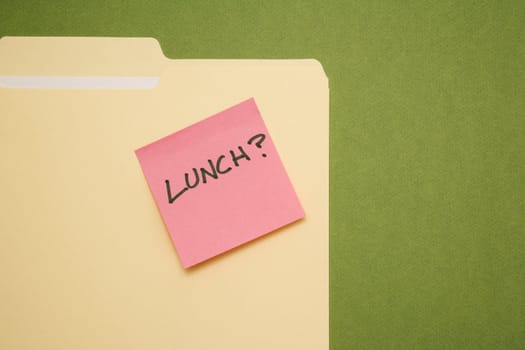 Folder with pink sticky note reading lunch on a green background.