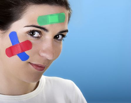 Beautiful woman with colored bandages on the face over a blue background