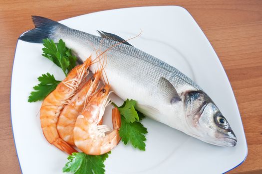 plate with sea bass, prawns, and parsley isolated on wooden background