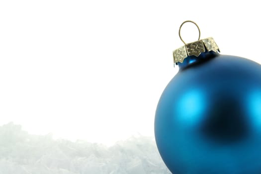 A blue Christmas bauble sitting in a bed of snow.
