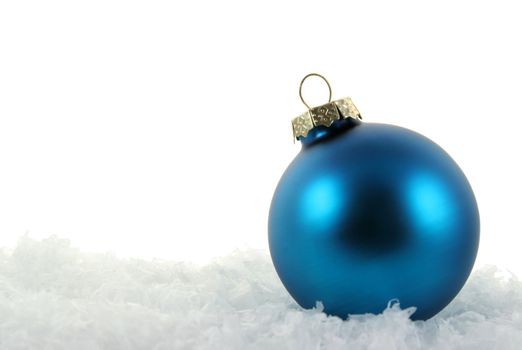 A blue Christmas bauble sitting in a bed of snow.
