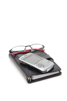 Closed Black Planner, with a silver PDA and glasses on top. On white.