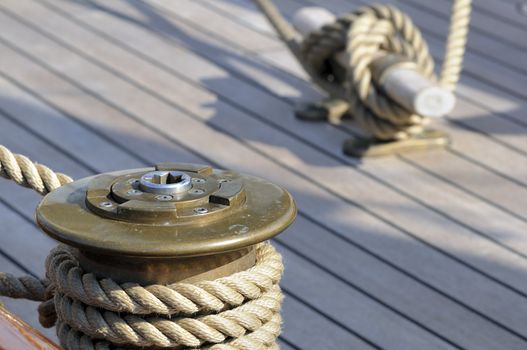 Close up of a sailboat deck: wrapped rope on a winch with a bitt in background 