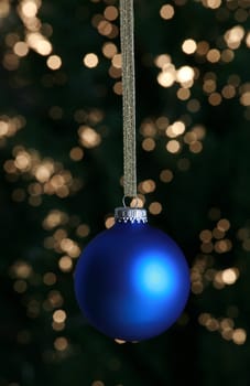 Blue Christmas ornament hanging against lit Christmas tree