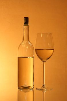 Wineglass near bottle of white wine with reverberation on red-yellow background