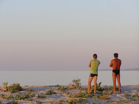 two men stand on the shore Azov sea and look at the sunset 