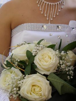 There is wedding bouquet of the white roses in the hands of bride. 