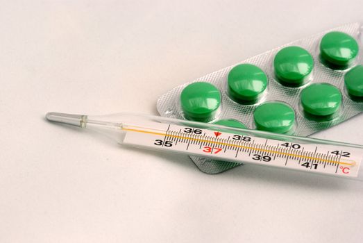 The medical thermometer and green tablets on a light grey background