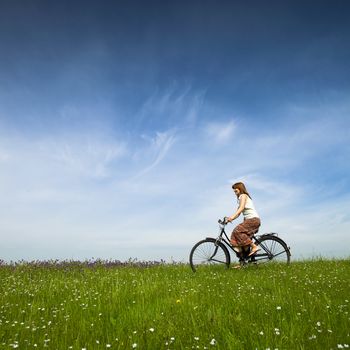 Happy young woman on a green meadow riding a bicycle