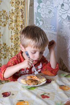 The little boy eats with a plug macaroni with a cutlet