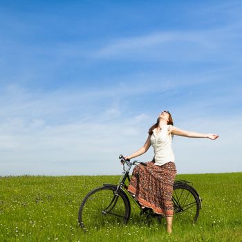 Happy young woman with a vintage bicycle on a green meadow