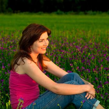 Beautiful young woman sitting on a flowery meadow