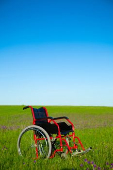 Concept image with a wheelchair abandoned on a green meadow, 