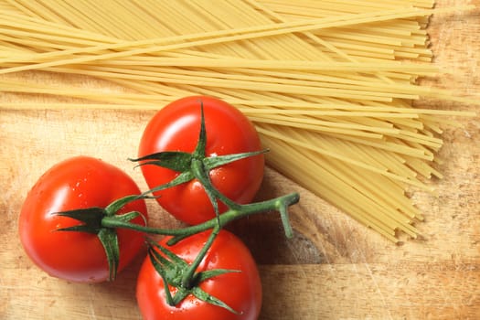 Raw spaghetti and few fresh tomatoes lying on wooden board