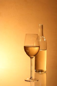 Wineglass near bottle of white wine with reverberation on red-yellow background