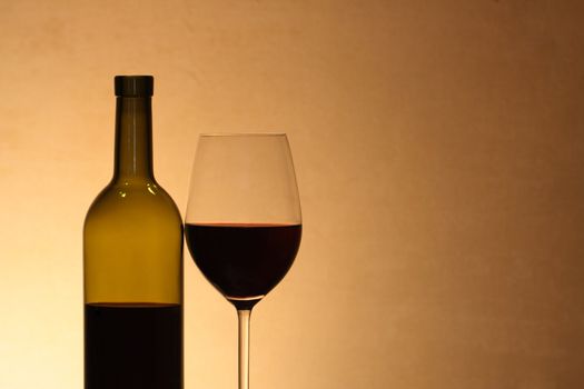 Wineglass near bottle of red wine with reverberation on brown background