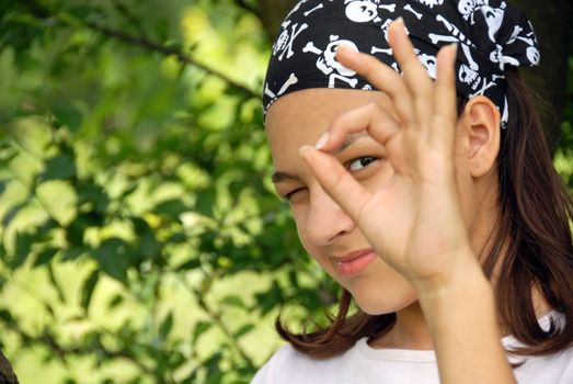 smiling teenage girl looking through ok sign over green natural background