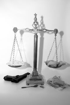 an antique scales against a white background with drugs and gun depicting drug crime