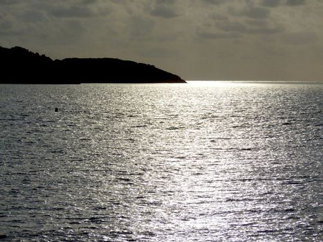 Black shadow of an island sirrounded by the sea with sun reflections by sunset