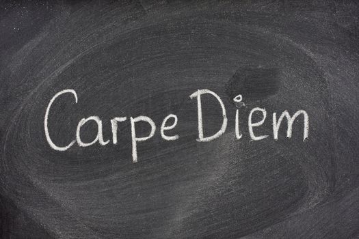 Enjoy life before it's too late, existential cautionary Latin phrase, Carpe Diem, a quote from Horace, handwritten with white chalk on blackboard.