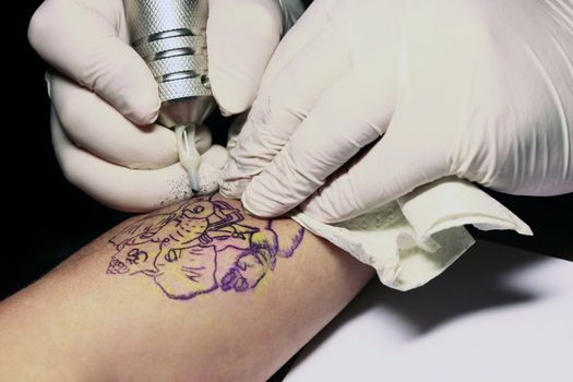 A tattoo artist applying his craft onto the hand of a female