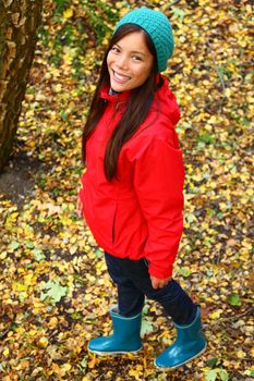 Autumn woman happy and smiling looking up at camera during a walk in the forest during fall