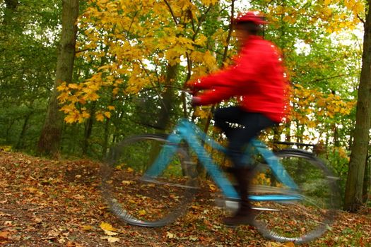 Woman biking in the autumn forest. Motion blurred bike.