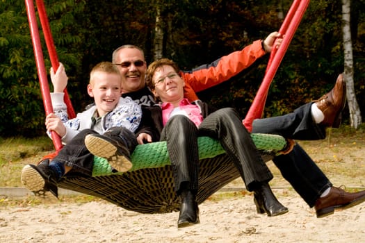 Happy young family in the swing on the playground