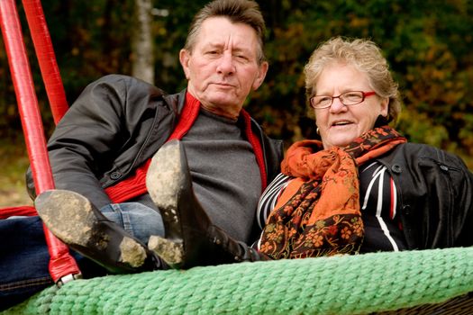 Happy older couple in the swing on the playground