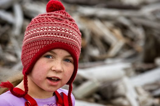 girl with red/white stocking cap, freckles, on wood covered beach