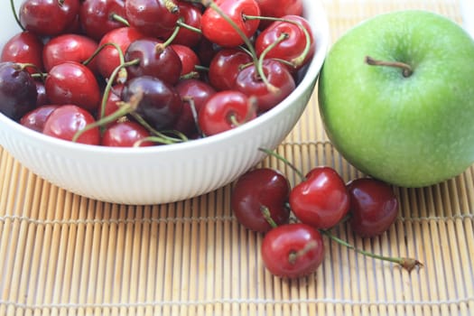A group of juicy, fresh cherries in a white bowl and a green apple