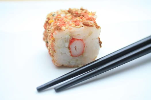 A piece of seame seed sushi and a pair of chopsticks