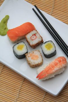 An oblong Japanese plate, serving a variety of sushi: Nigirisushi, rice with a raw fish topping and Makisushi, rice wrapped in a thin slice of seaweed, called nori. As condiment some hot green wasabi is served on the plate