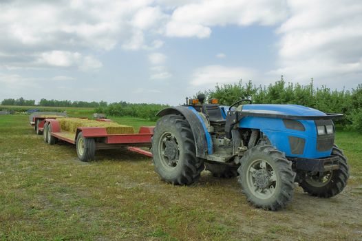 a trailor with haystacks attached to a blue tractor