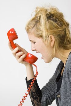 young teenage girl yelling into red vintage telephone receiver