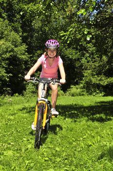 Portrait of a teenage girl riding a bicycle in summer park outdoors