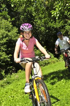 Teenage girl and her father riding bicycles in summer park