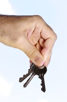 Man's hand holding house keys on blue sky background