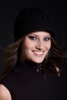 Beautiful brunette with a winter hat on on black background with gorgeous smile