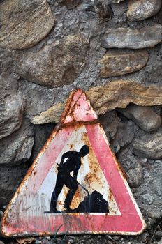 Old, rusty roadworks sign in front of rough and ancient stone wall