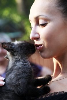 The young beautiful dark-haired woman holds in hands of a black kitten.